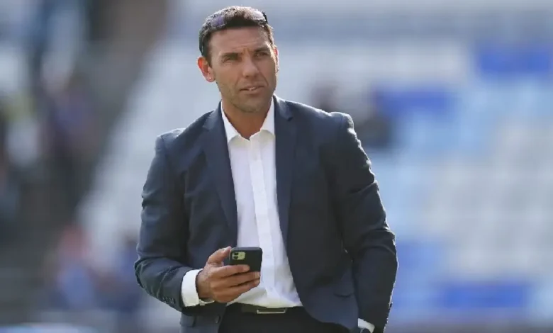 Damián Zamogilny, con traje azul oscuro y camisa blanca, sostiene un teléfono móvil mientras camina en un estadio; su expresión es seria.